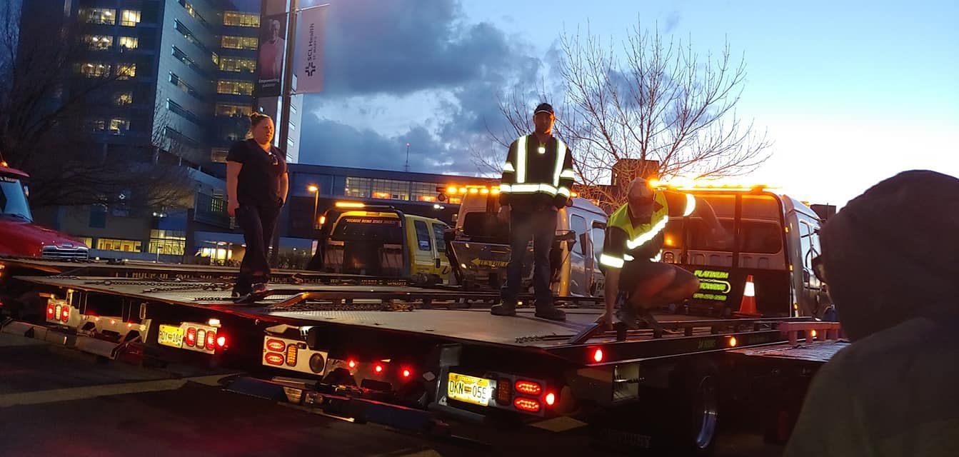 Tow truck workers in reflective gear loading a car at dusk beside a damaged vehicle and flashing lights