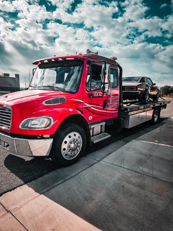 Red flatbed tow truck on a street under a cloudy sky, carrying a black car.