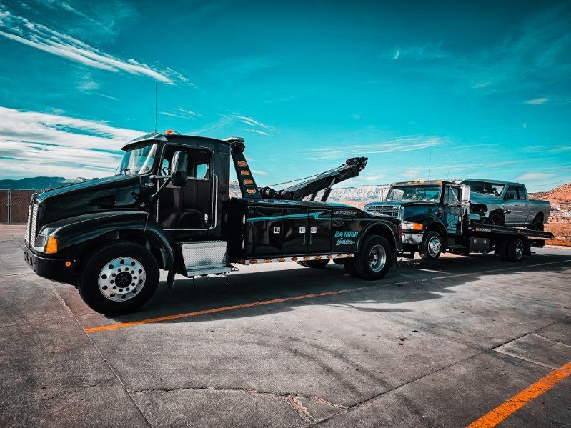 Two black tow trucks parked side by side on a road under a bright blue sky.