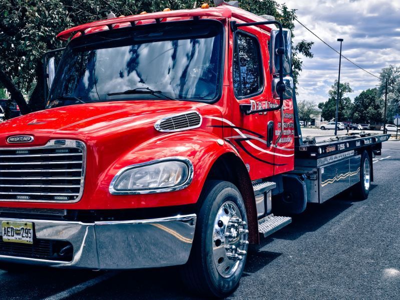Red flatbed tow truck parked on a street under a cloudy sky.