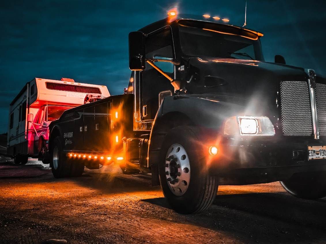 Black semi-truck hauling a red trailer on a road at dusk with amber lights glowing