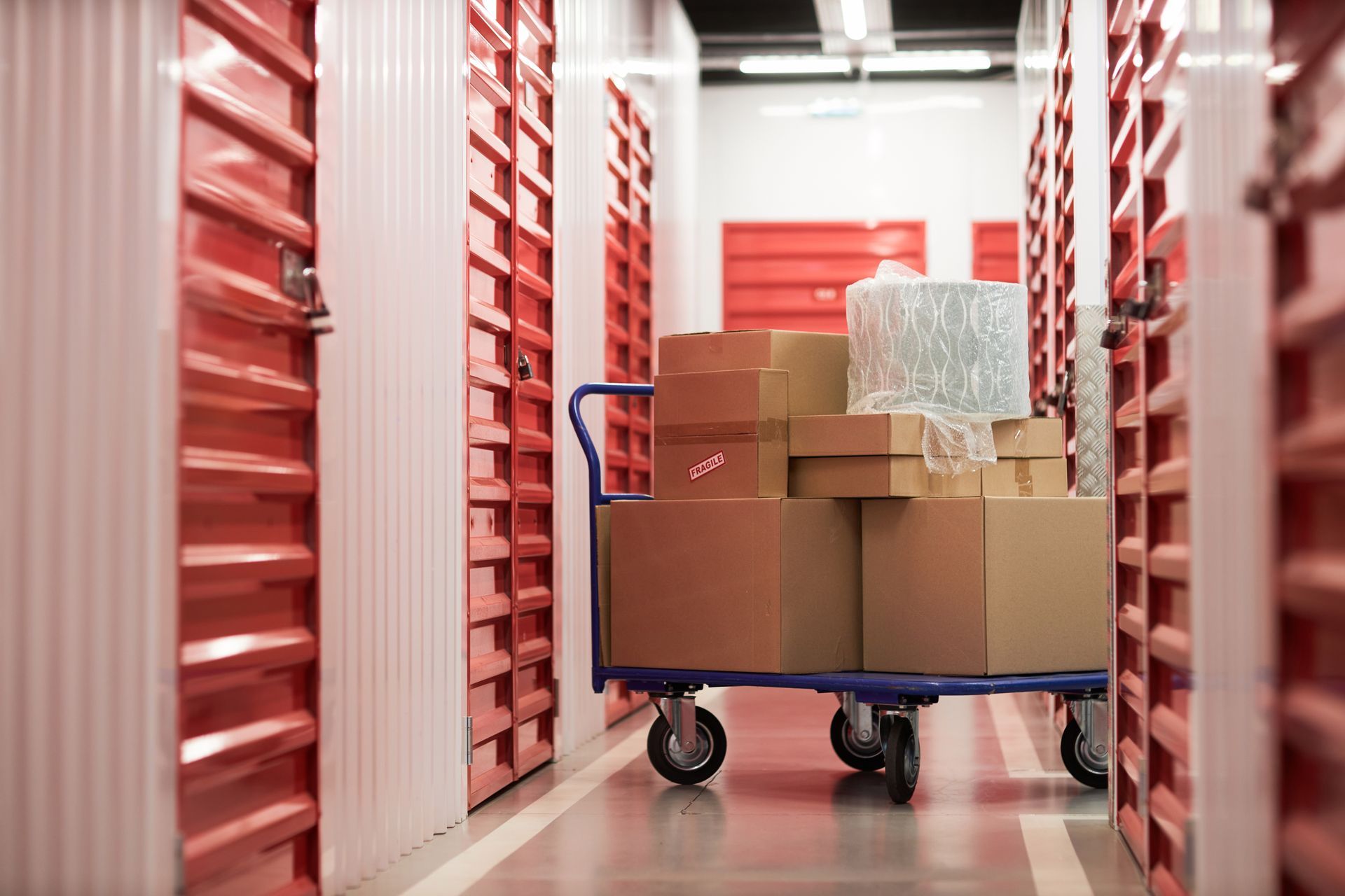 Red storage units in a hallway; a cart loaded with cardboard boxes and wrapped items.