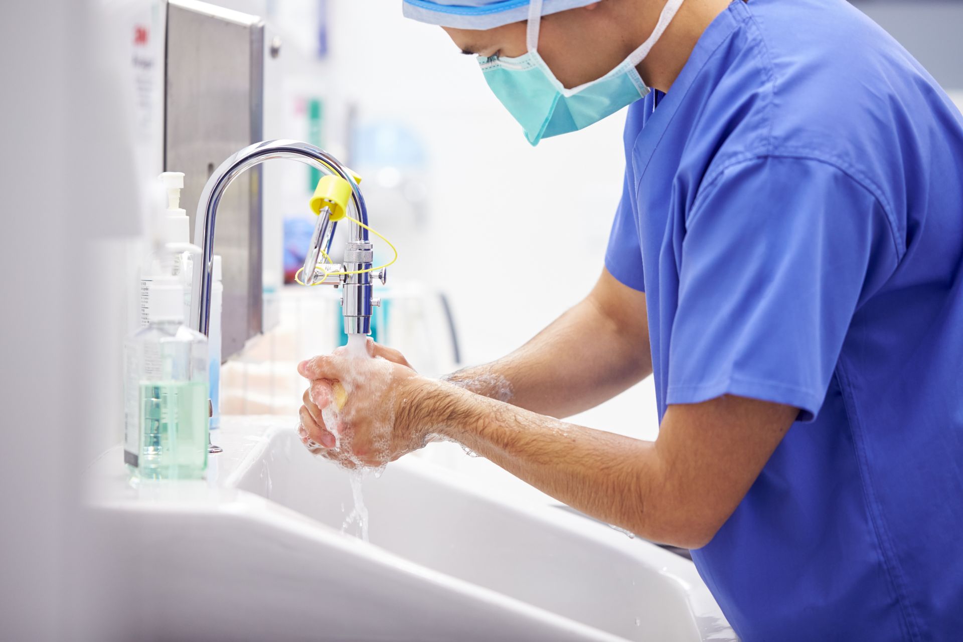A surgeon is washing his hands in a hospital sink.