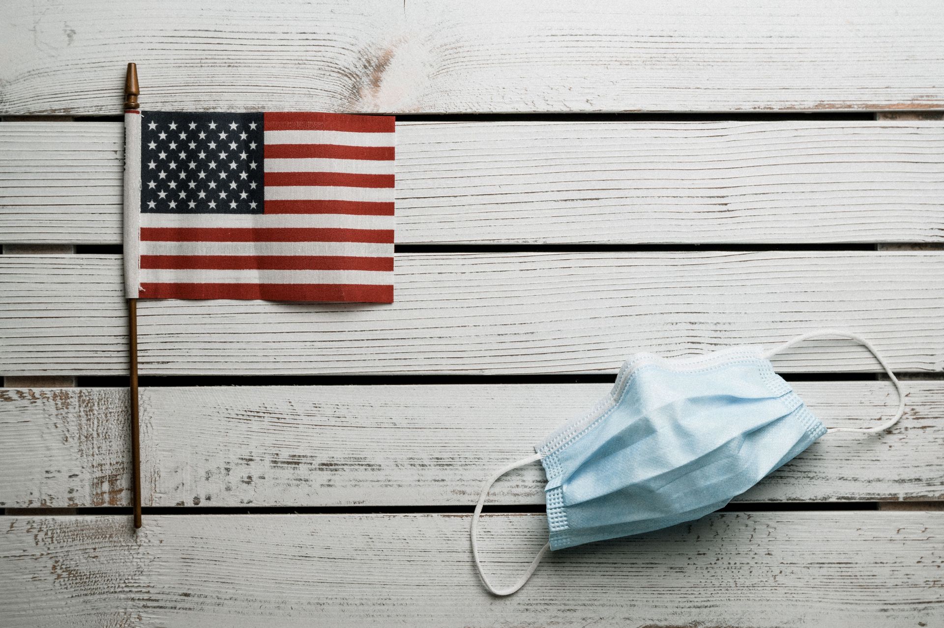 American flag and blue face mask on weathered white wooden planks