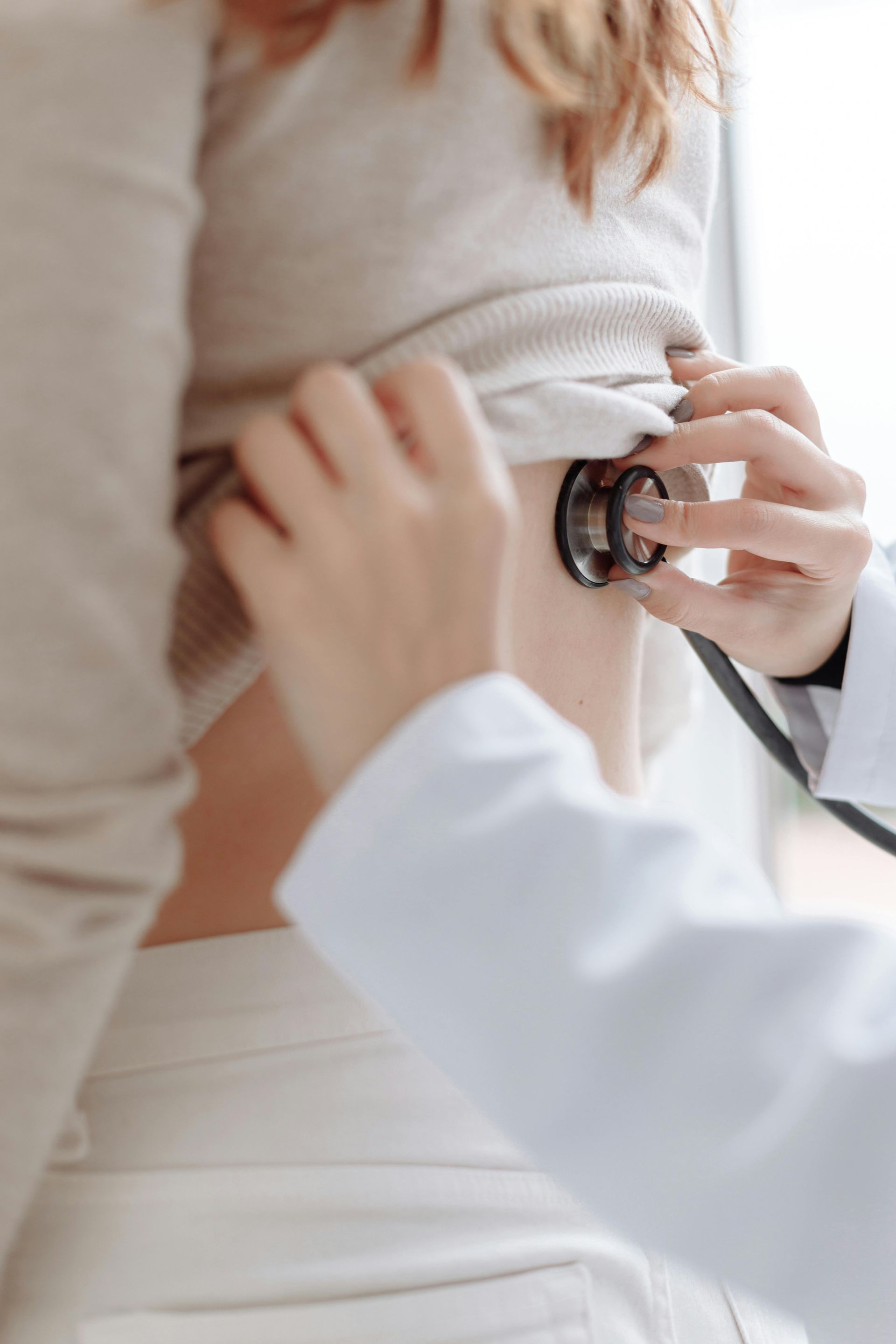 Doctor using a stethoscope to examine a patient's chest in a bright clinic
