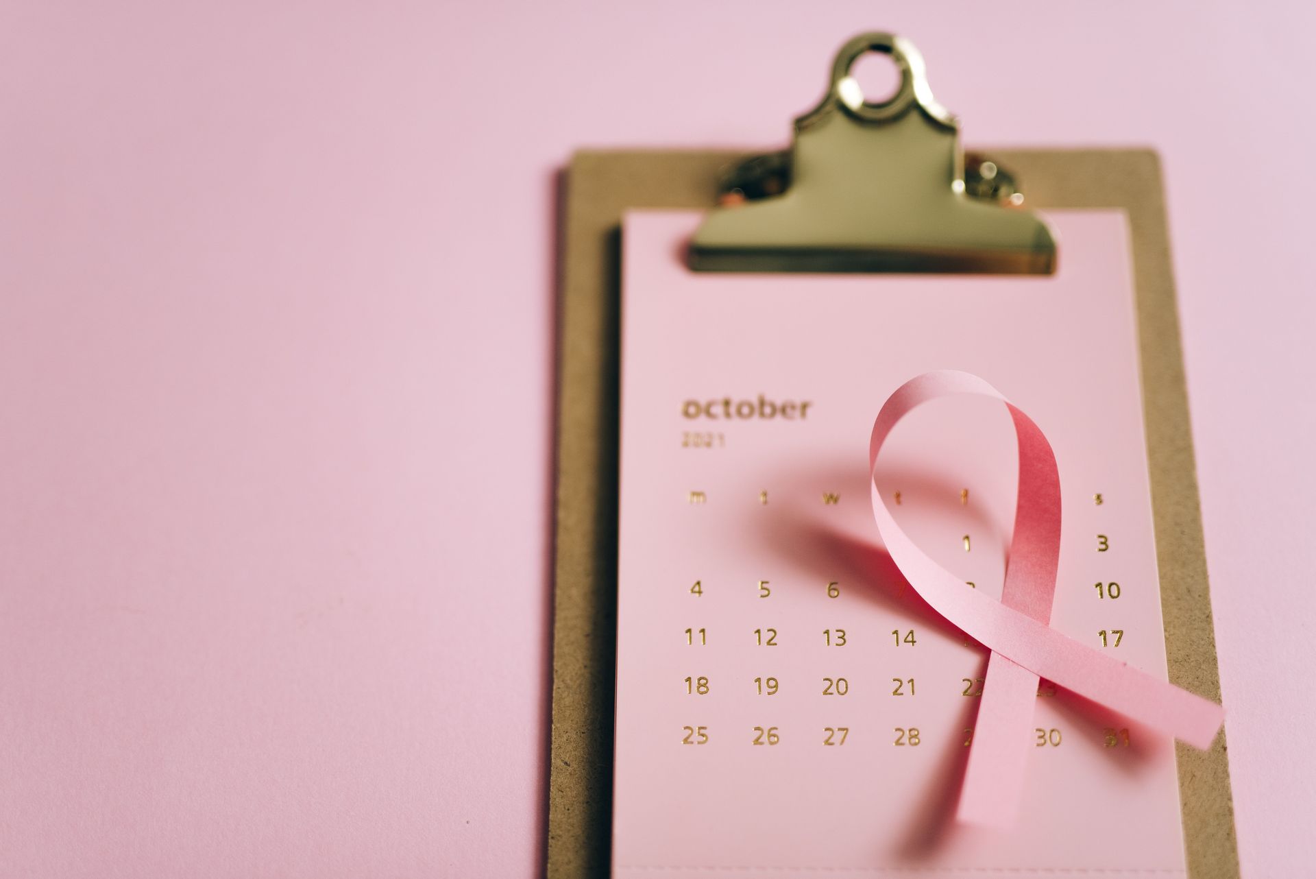 Pink awareness ribbon on a clipboard calendar showing October.