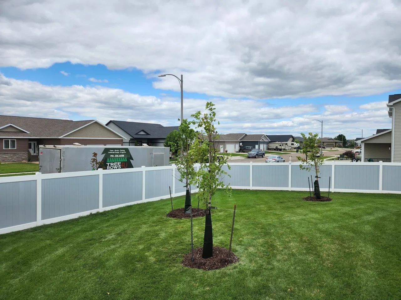 A backyard with a white fence and trees in the middle of it.