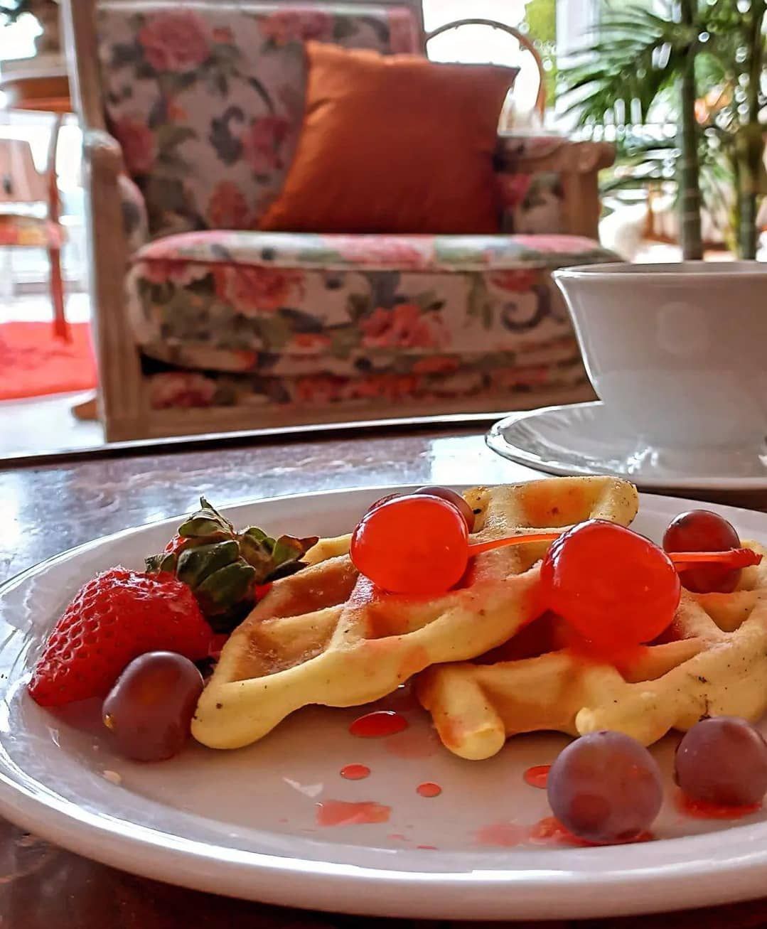 Um prato de waffles com morangos e uvas sobre uma mesa.