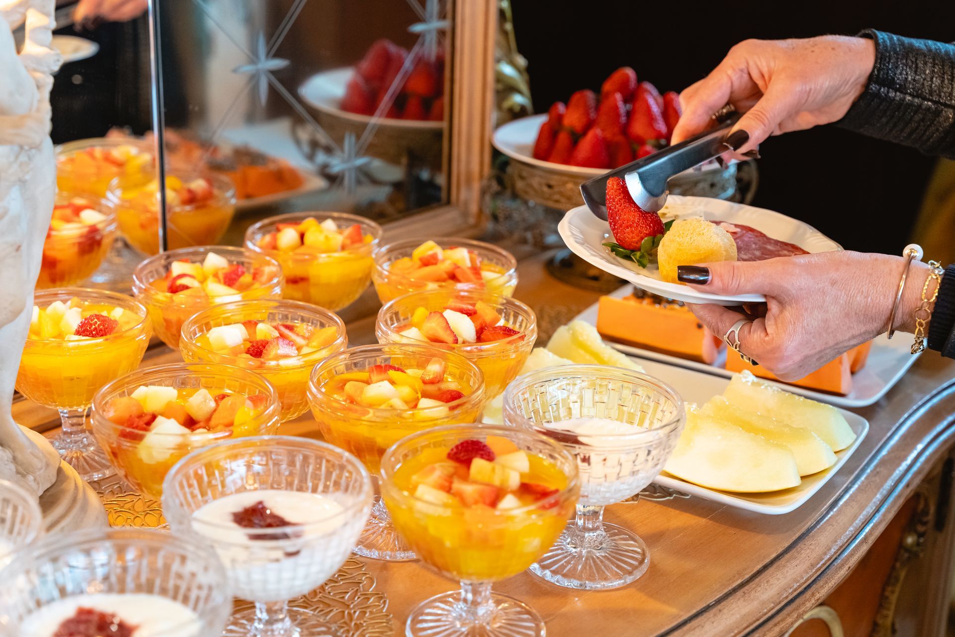 Uma pessoa está pegando um prato de frutas de uma mesa de bufê.