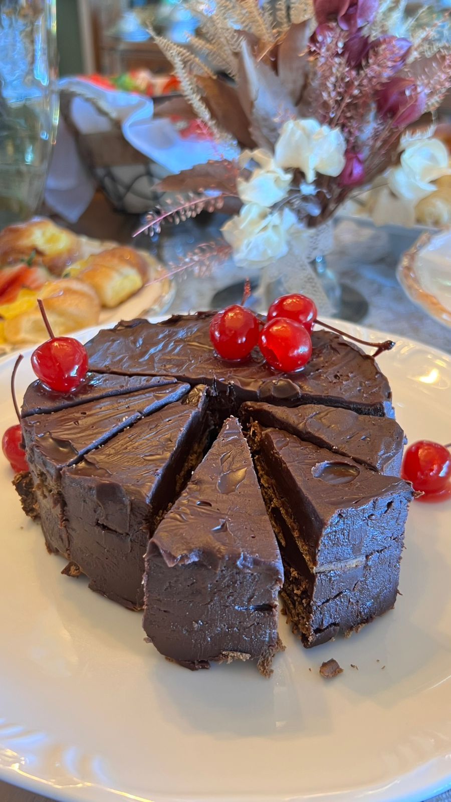 Um bolo de chocolate com cerejas por cima está em um prato branco.