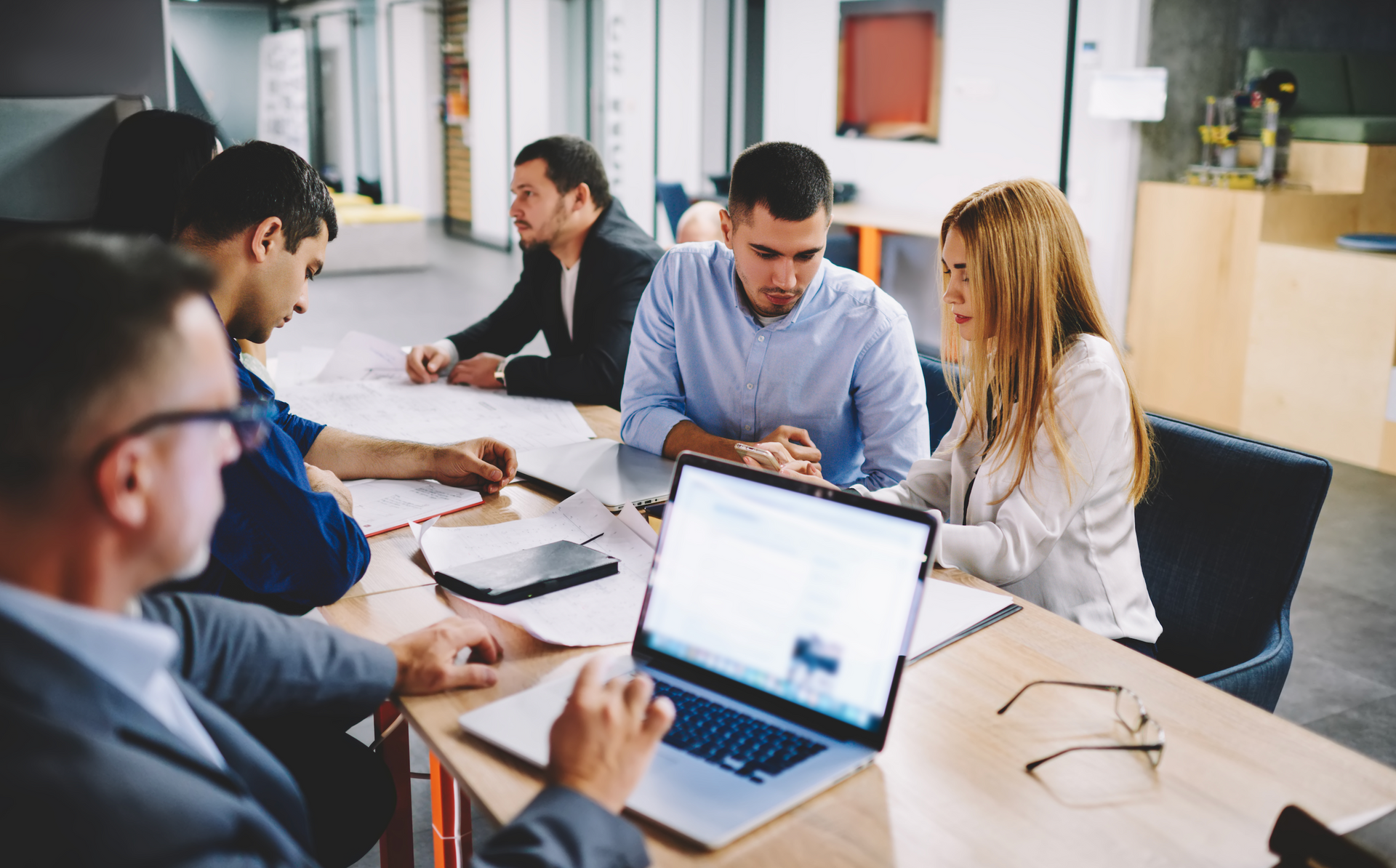 A group of people are sitting around a table with laptops.