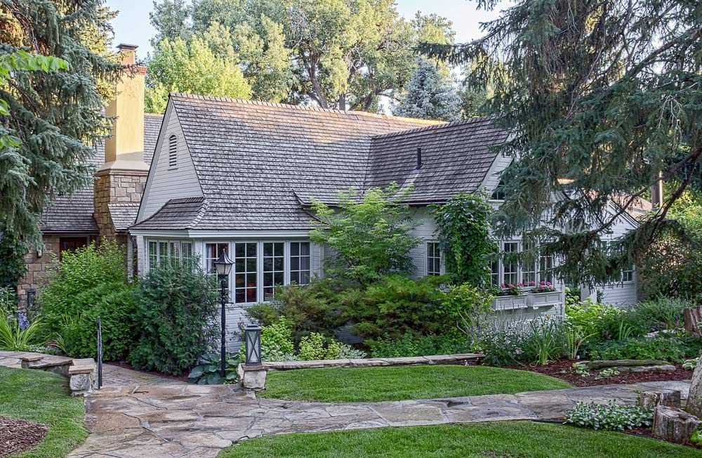 Charming gray house with a shingled roof, front garden, and stone walkway surrounded by greenery.