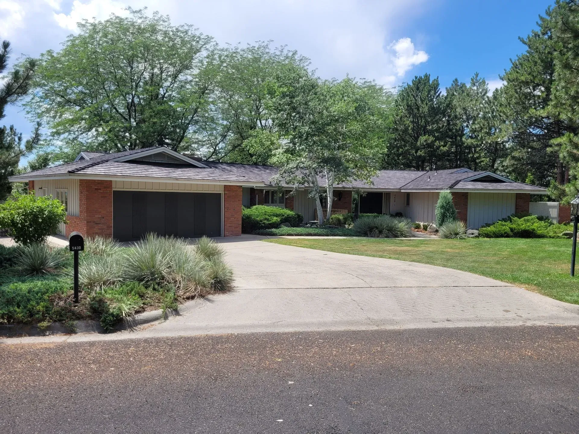 Suburban house with brick garage, curved driveway, and lush green trees under a blue sky