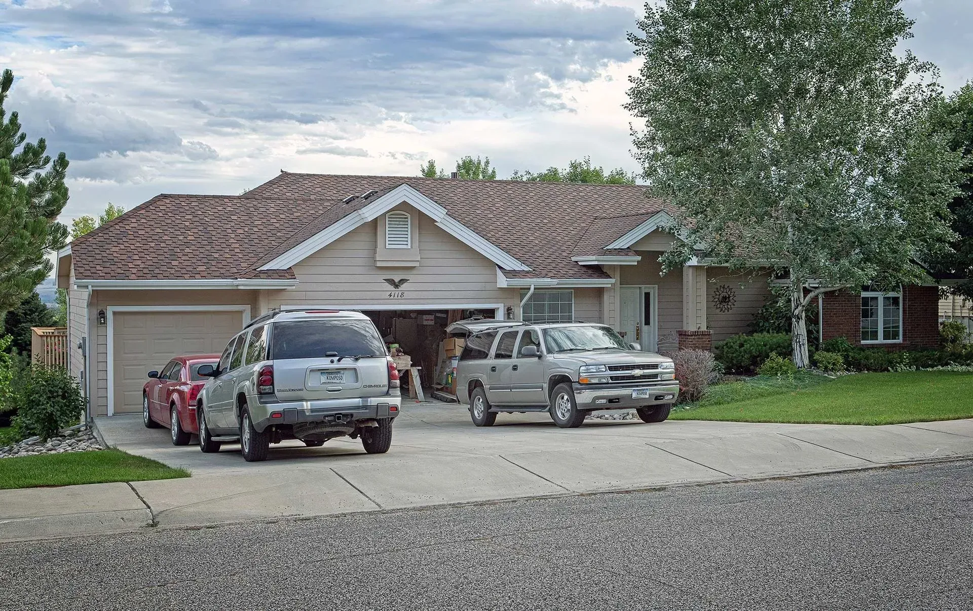 Suburban house with three parked vehicles on a driveway under a cloudy sky