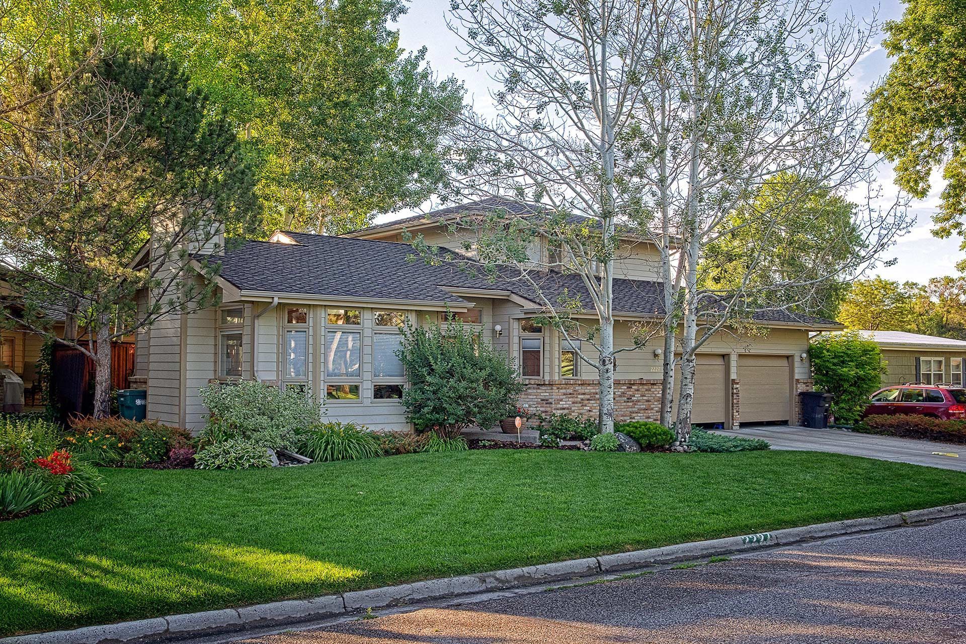 Single-story suburban house with a green lawn, mature trees, and a garage on a quiet street