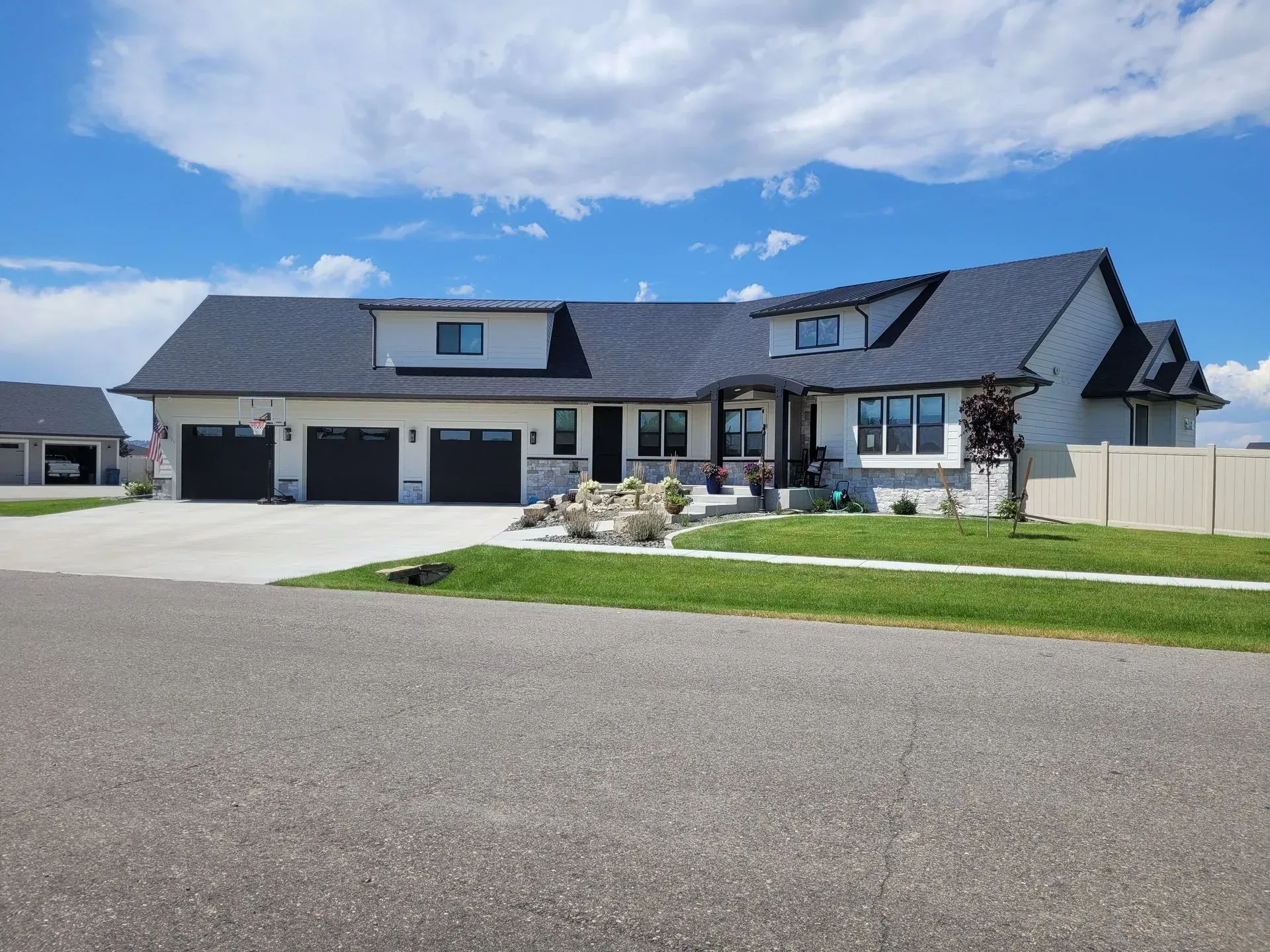 Modern single-story house with dark roof, three-car garage, and landscaped front yard under a blue sky