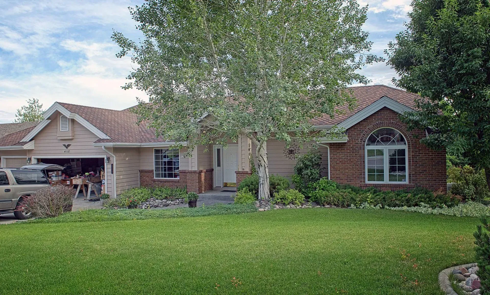 Single-story brick house with a large tree and green lawn in front
