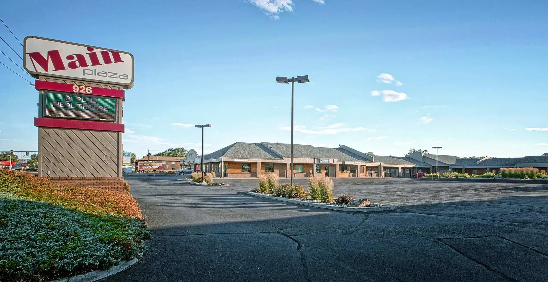 Shopping center parking lot with a Main Street sign, storefronts, and a clear blue sky