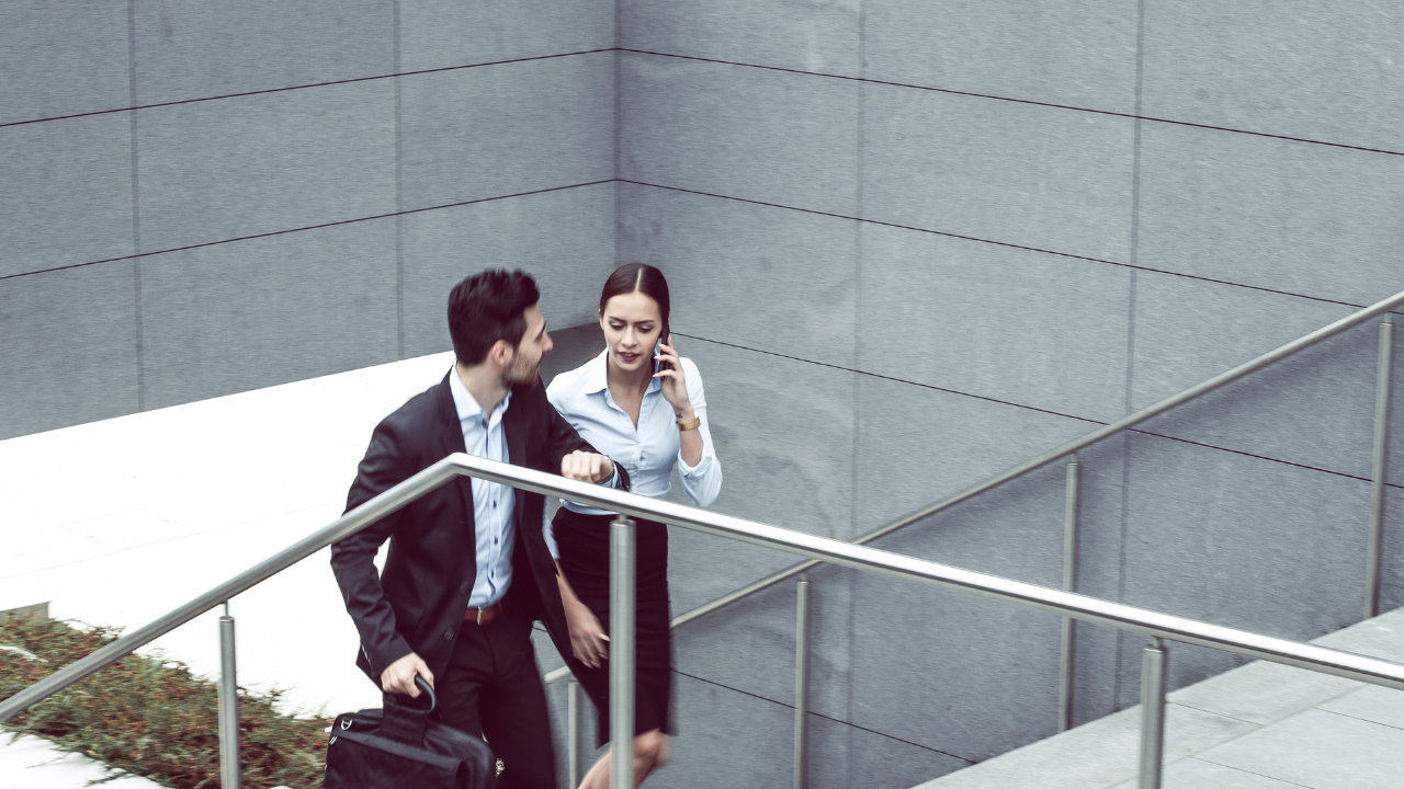 Two people walking on a stairway beside a gray concrete building, talking together.