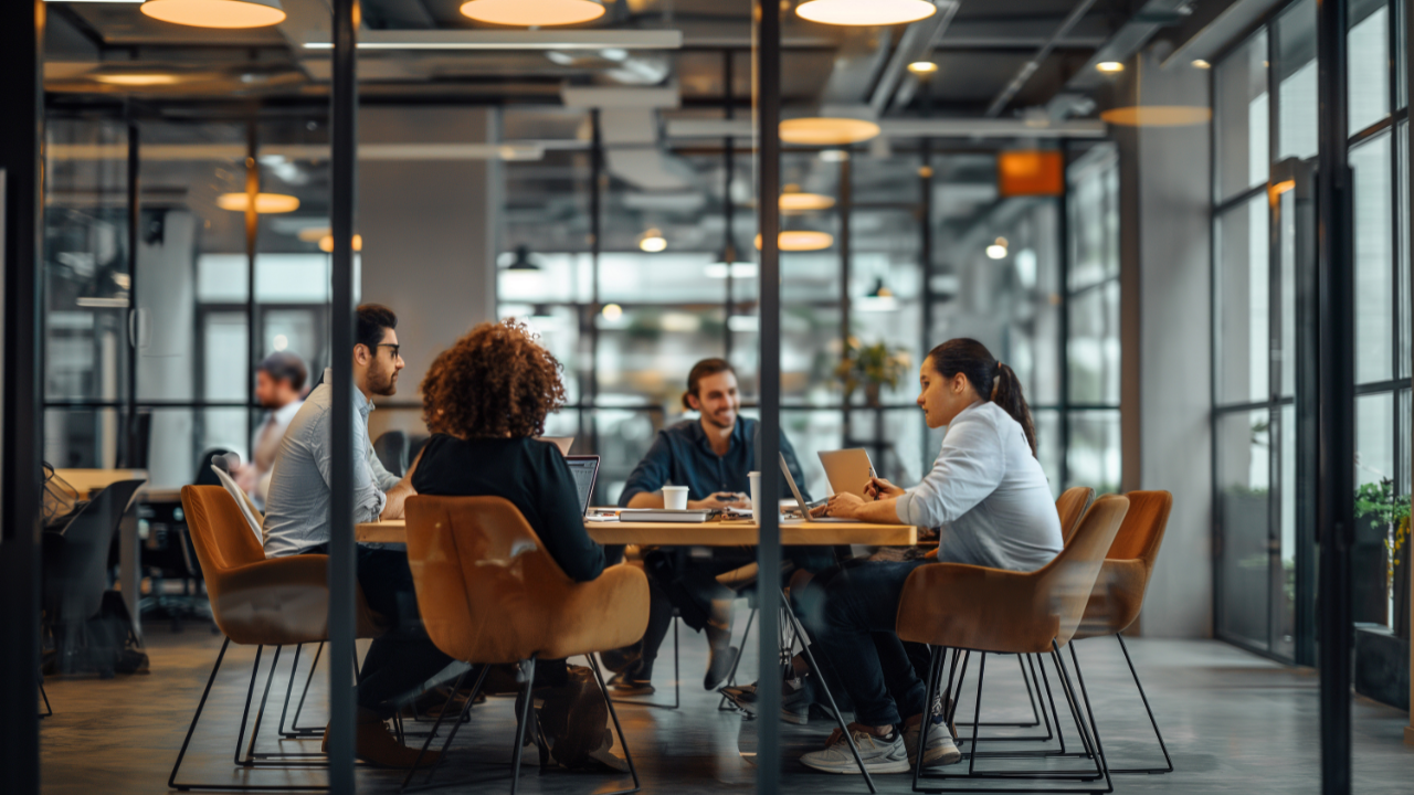 People in a glass-walled conference room discussing around a table in a modern office