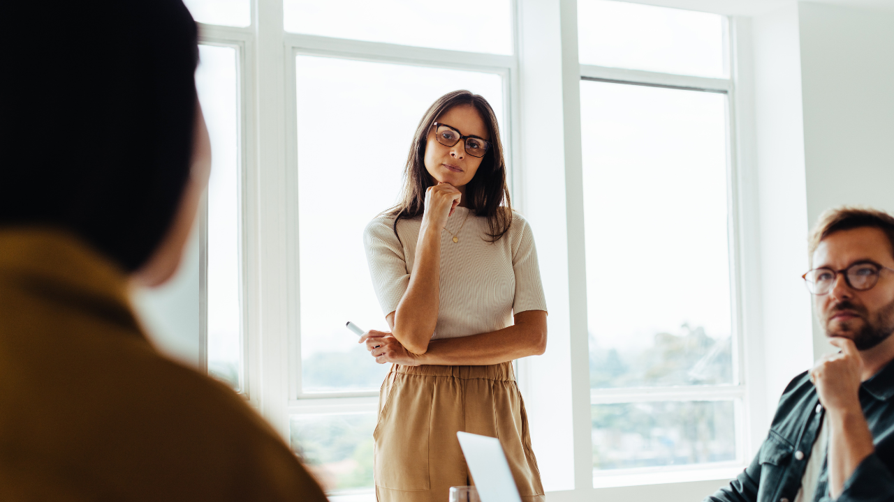 Two people listening to a woman speaking in a bright office meeting room