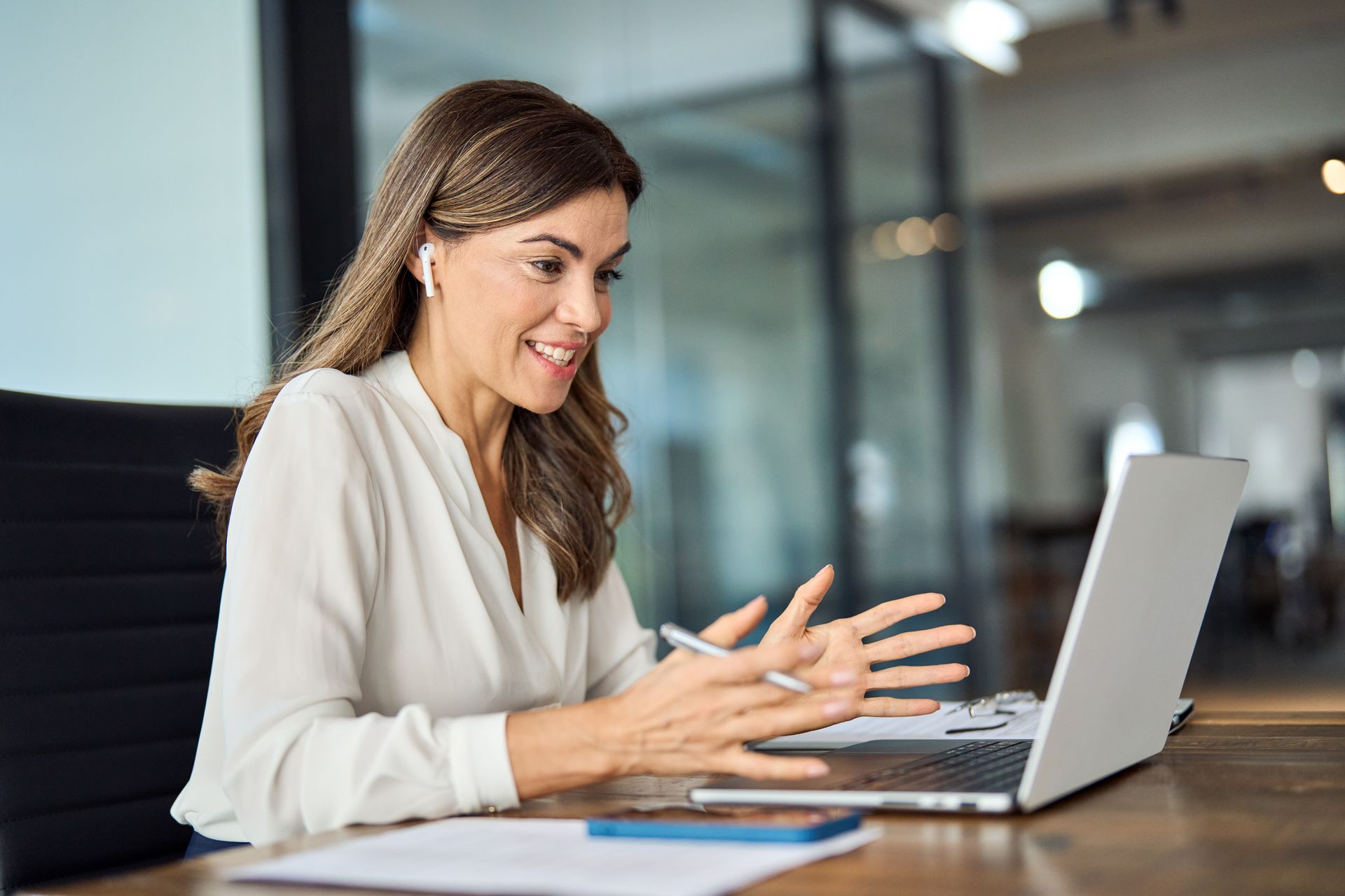 Woman smiling and gesturing while working on a laptop at a desk in an office