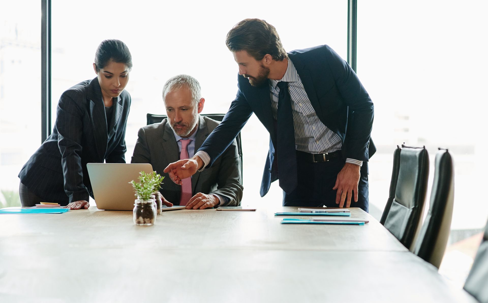 Three colleagues in business attire discussing documents around a conference table in a bright office