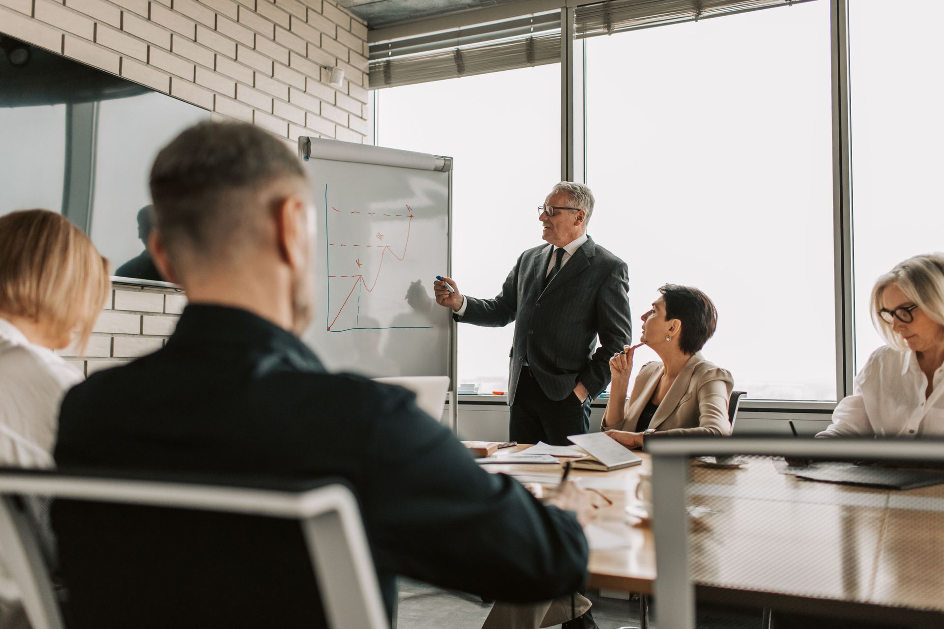 Business meeting with five people around a conference table, focused on a man speaking at the head of the table.