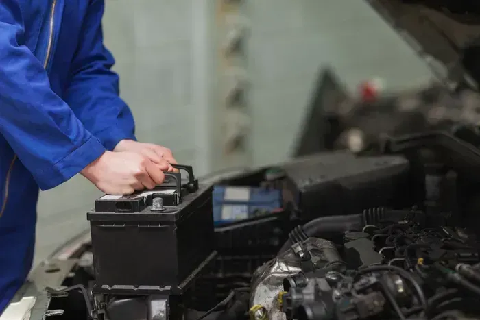 Mechanic in blue jacket checking a car battery in an engine bay
