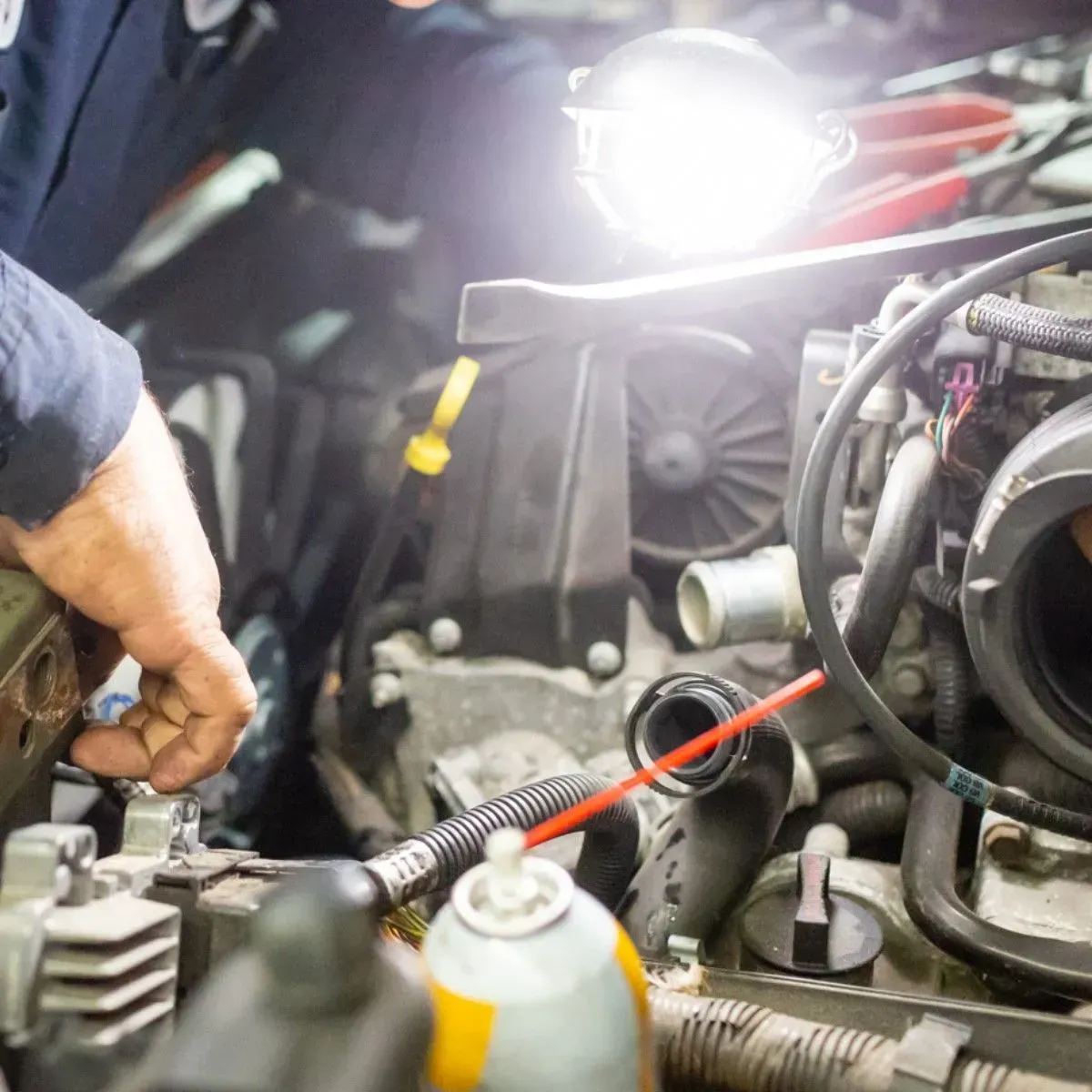 Mechanic working on car engine with bright work light in a garage