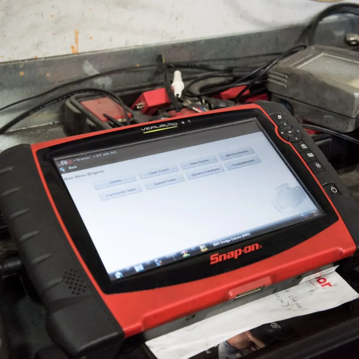 Red Snap-on diagnostic tablet on a workbench with cables and tools around it