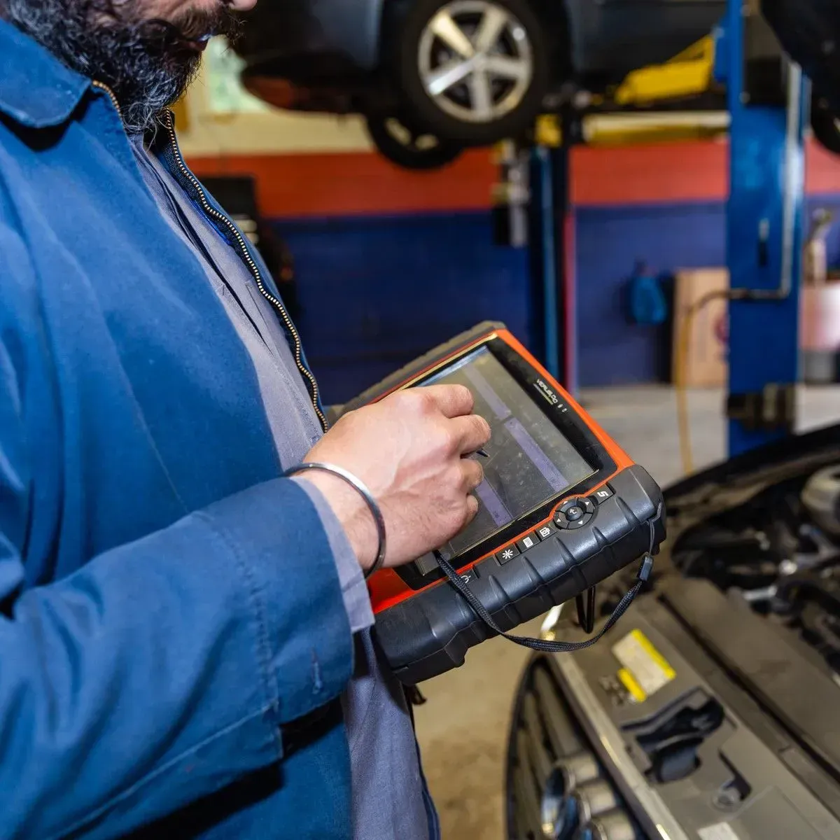 Mechanic using a diagnostic tablet under a car in an auto repair shop