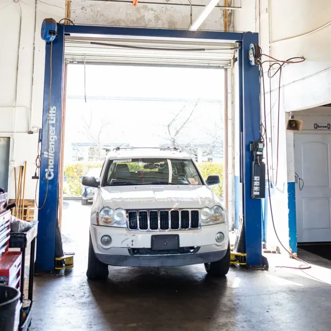 White SUV inside a blue two-post vehicle lift in an auto garage, front view.