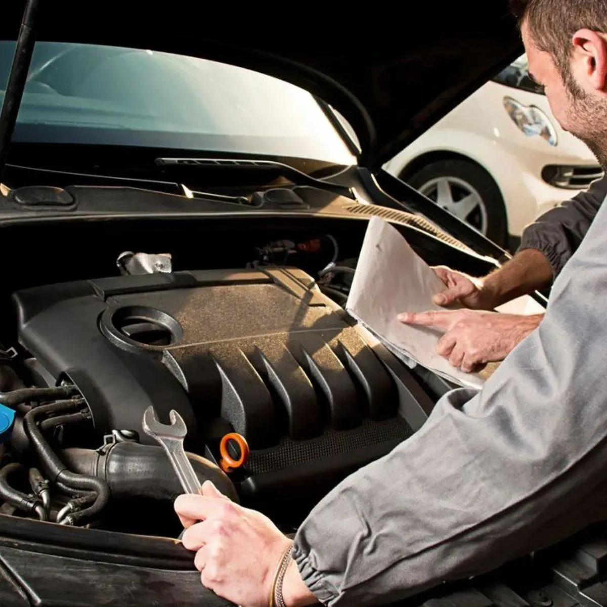 Mechanic inspecting a car engine under the hood with a clipboard in a garage