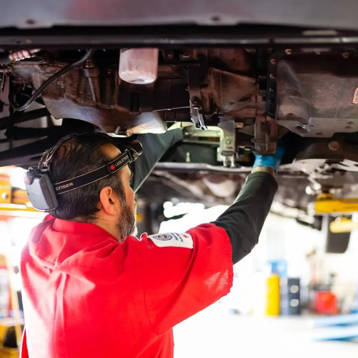 Mechanic in red jacket working under a raised car in an auto repair shop