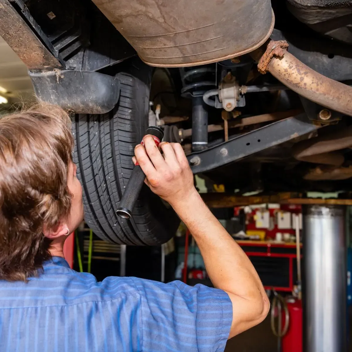 Mechanic inspecting a car’s undercarriage and tire on a lift in an auto repair shop
