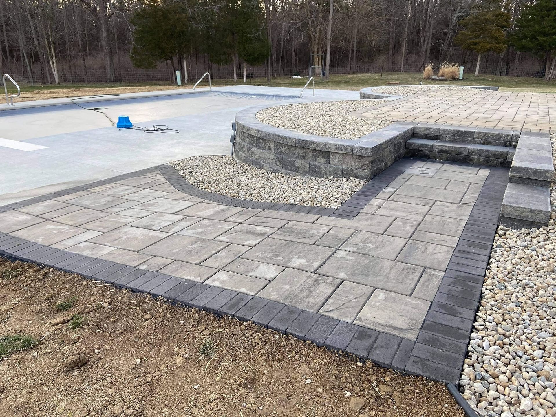 Multi-level paver patio walkway with integrated concrete block steps next to a residential swimming pool.