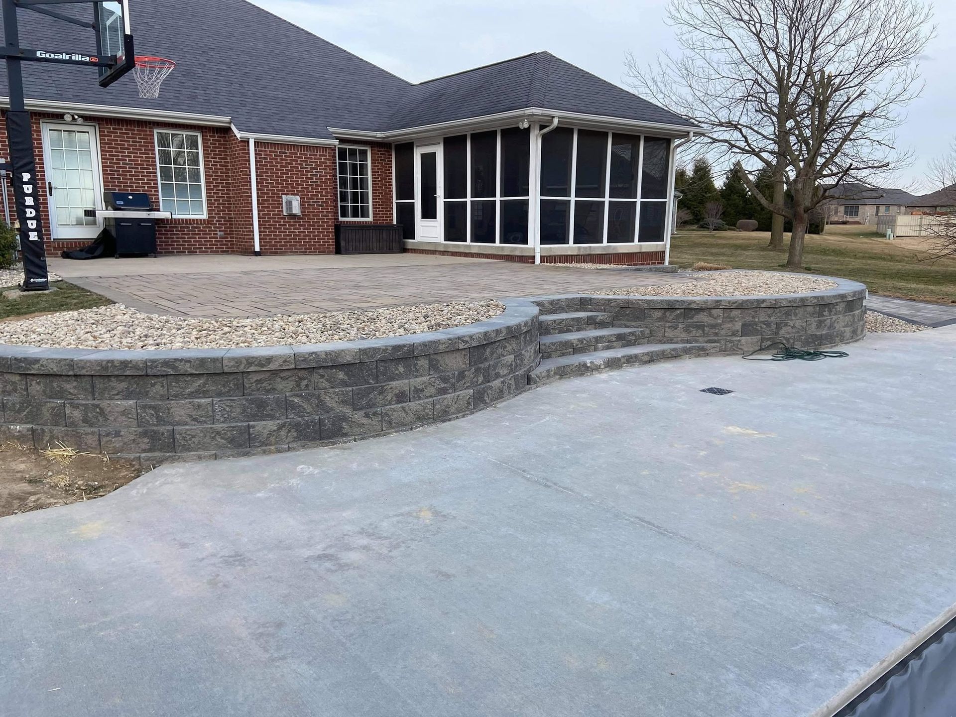 Tiered stone block retaining wall supporting an elevated brick house patio area with built-in steps.
