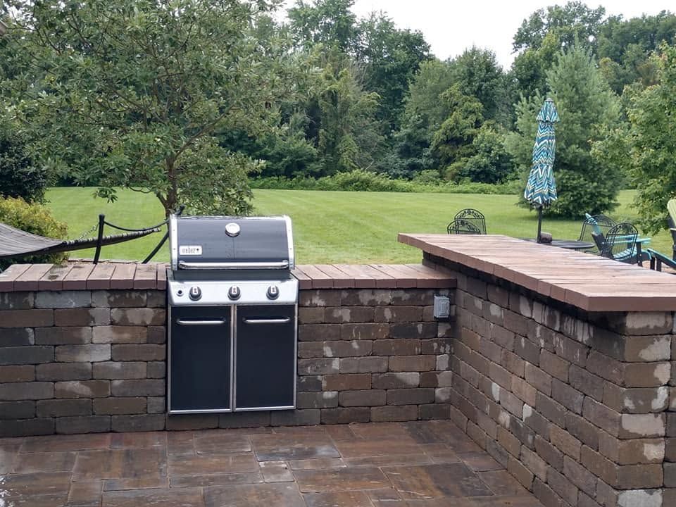 Outdoor brick kitchen structure with a built-in grill overlooking a spacious green lawn