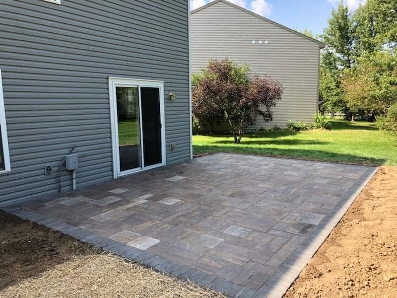 Newly completed stone paver patio extending out from a home's sliding glass backdoor