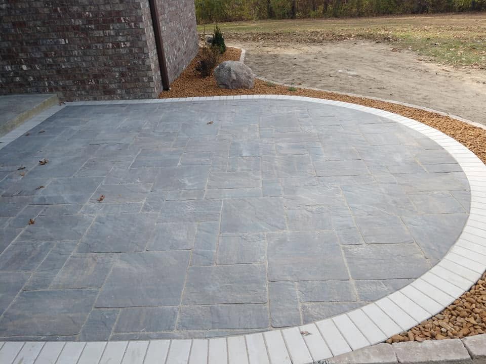Completed circular paver patio installation featuring stone block edging and a river rock landscape bed.
