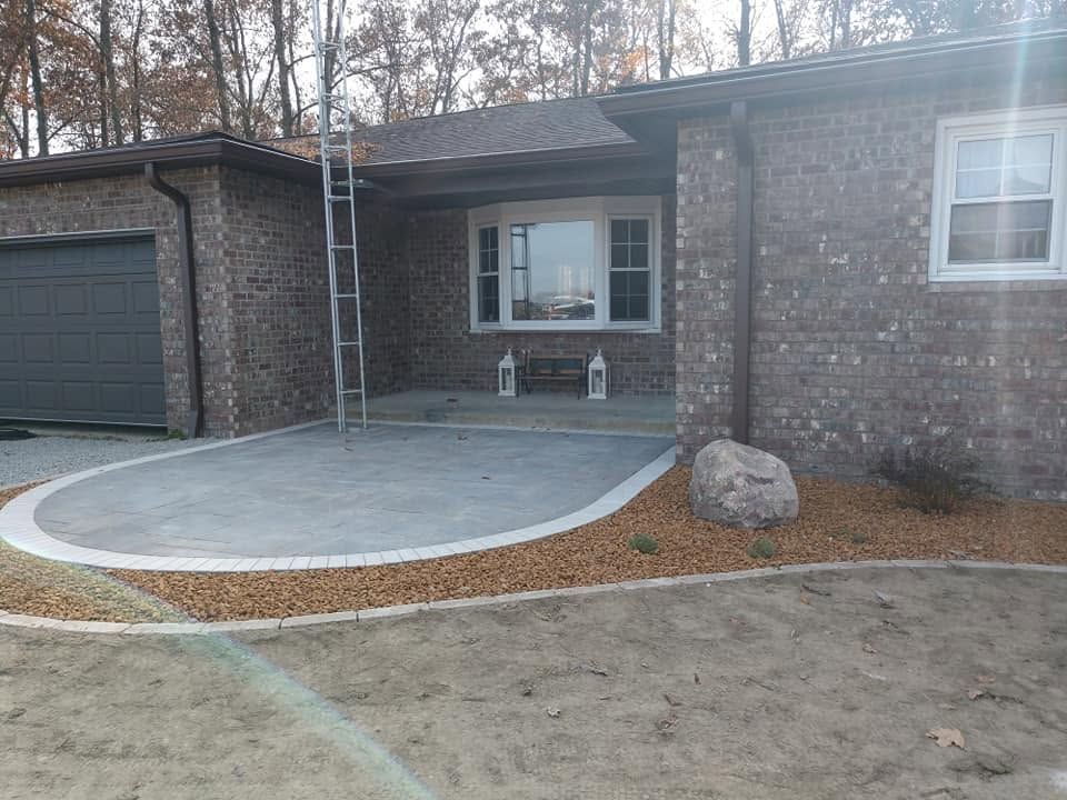 Curved paver patio design with a decorative gravel border next to a brick home.