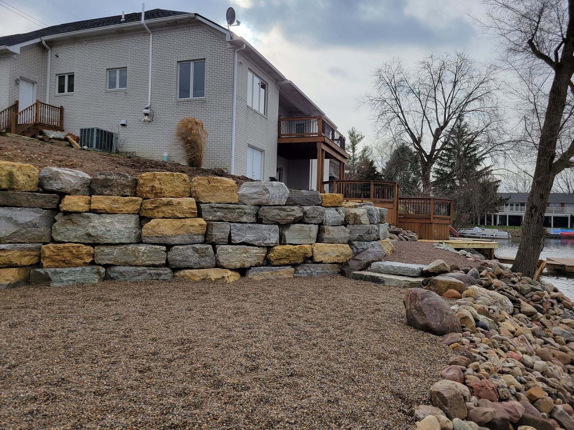 House on a terraced stone retaining wall beside a gravel yard and leafless trees