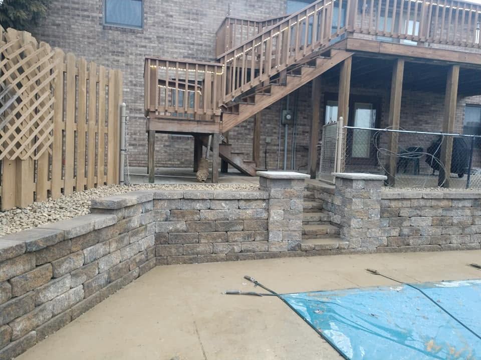 Backyard patio with stone retaining walls, wooden deck stairs, and a covered pool