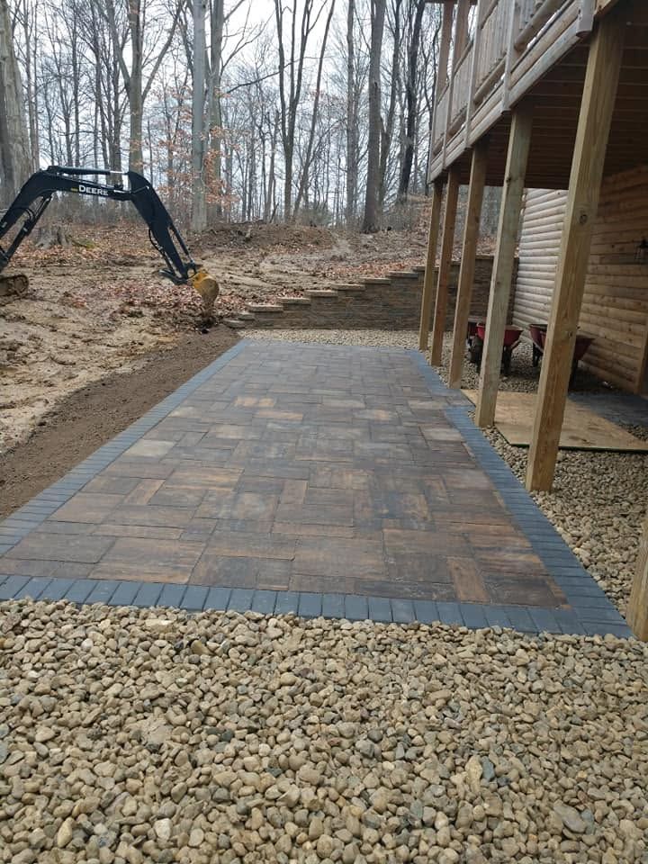 Backyard stone paver patio installation with tiered block retaining wall under construction.