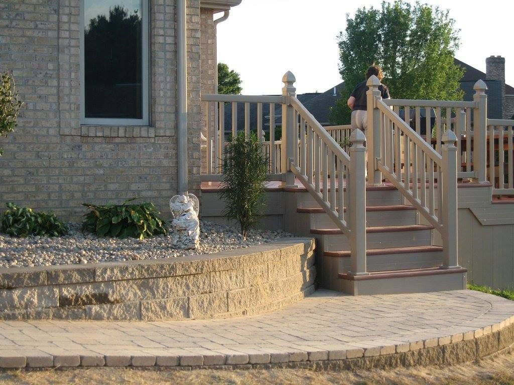 Curved gray stone retaining wall with a river rock landscape bed next to a wooden staircase and paver patio