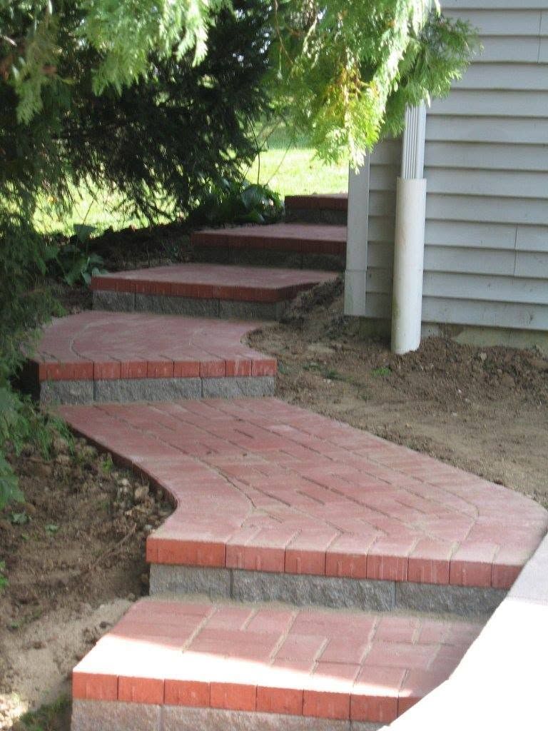 Stepped walkway made of red brick pavers with gray block risers leading up a slope next to a house