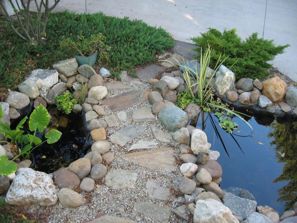 Natural stone and gravel pathway winding through a backyard water garden with river rock borders