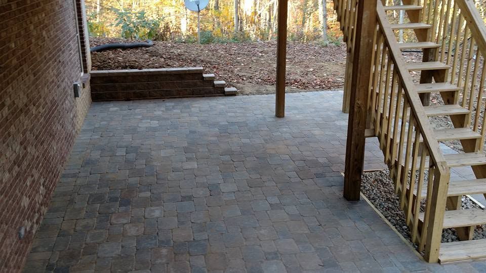 Completed paver patio installation beneath a deck with wooden stairs