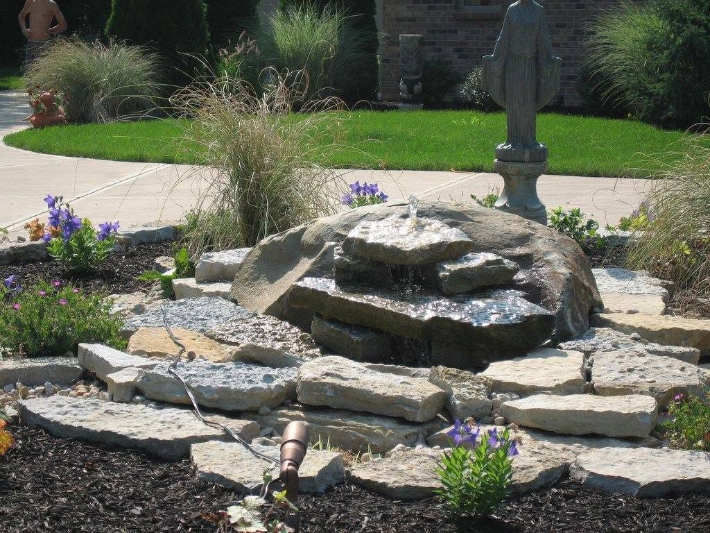 Tiered natural flagstone waterfall fountain feature with ornamental grasses and a garden statue